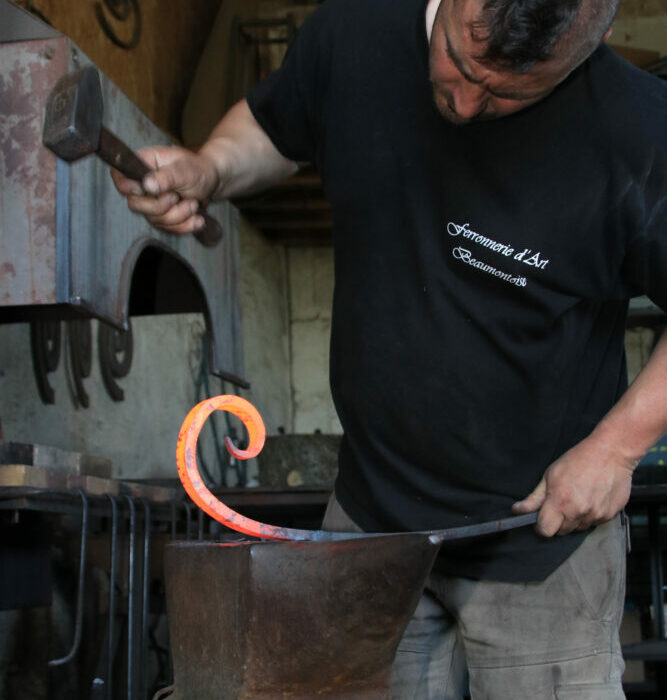 Antonin Noyer qui forge une volute en acier sur son enclume, avec son marteau